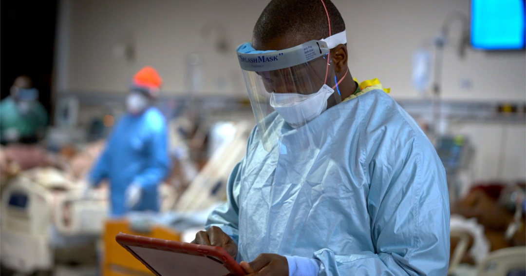 Photo of a healthcare worker, in scrubs and face mask and visor, in the foreground of patients in hospital beds. The photo is for an article about 50 ways to use FileMaker.