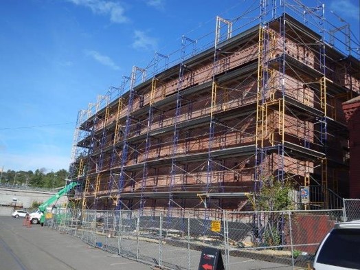 A building under construction with scaffolding built up around the walls and safety fences in front of the building.