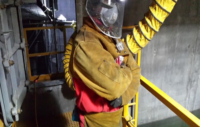 A construction worker in a yellow hazmat suit posing for a photo with his arms crossed across his chest.