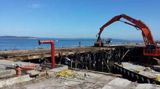 A construction site overlooking the ocean with a large bulldozer on the right hand side.