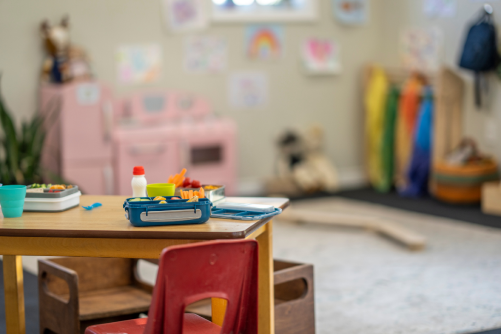 Photo of a daycare classroom, with a table and snacks in focus at the front of the photo. The blurred background shows a pink play kitchen, colorful scarves, and drawings pinned on the wall. This image helps to illustrate our FileMaker in education article.